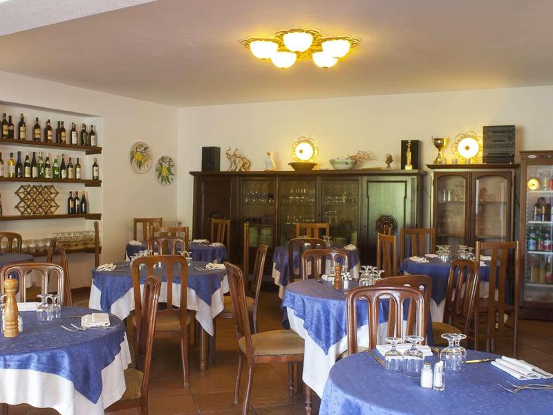 Kleines Restaurant mit blauen Tischdecken, Holzmöbeln, Wandregalen und warmem Deckenlicht.