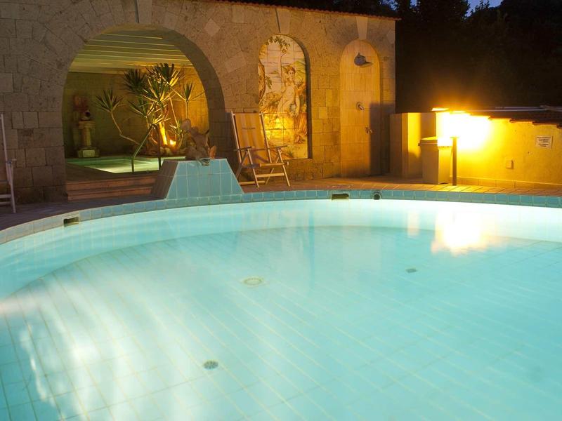 Beleuchteter Pool bei Nacht mit gemütlichem Sitzbereich und gelber Wandbeleuchtung.