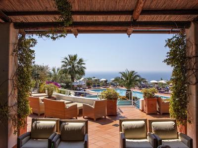 Terrasse mit bequemen Stühlen, Blick auf Pool, Palmen und das blaue Meer im Hintergrund.