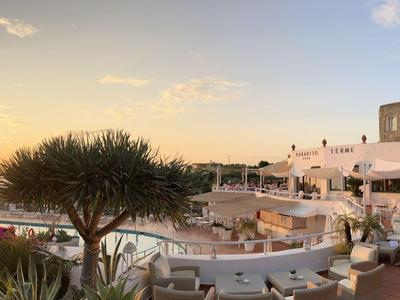 Sonniger Hotelterrasse mit Sitzbereichen, Blick auf Sonnenuntergang und Meer in Urlaubsidylle.