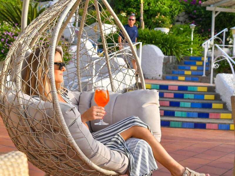 Osoba relaxuje v závěsném křesle na terase s barevnými schody v pozadí