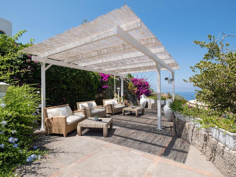 Sezení s pohovkami a pergolou v zahradě s výhledem na moře.