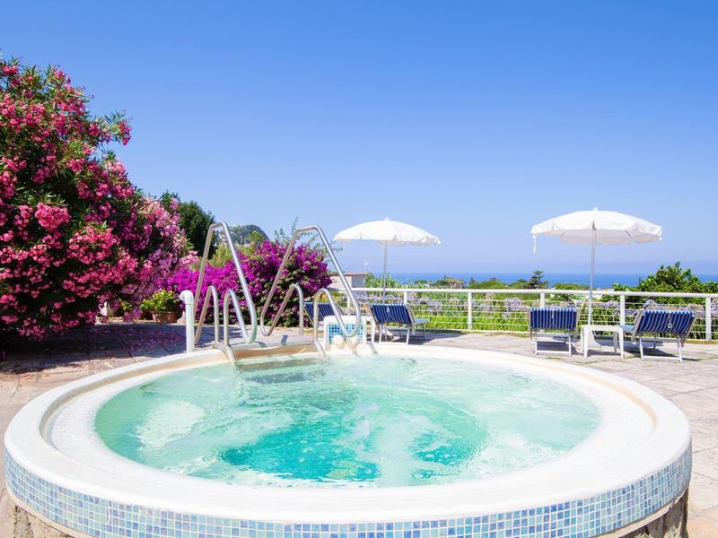 Kruhová venkovní vířivka s výhledem na moře a slunečníky za jasné oblohy.