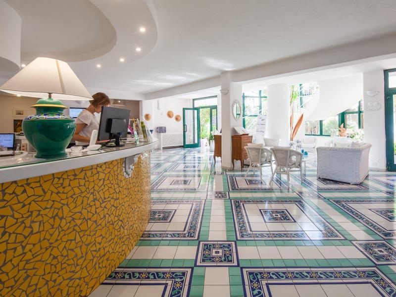 Světlá hotelová lobby s moderní recepcí a barevným vzorovaným podlahovým krytem.