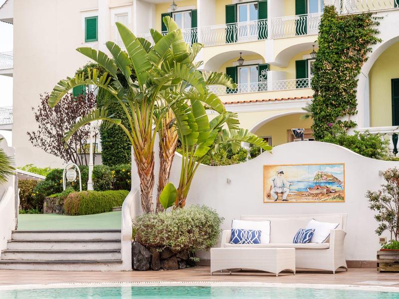 Panca bianca accogliente con cuscini blu vicino alla piscina davanti a un hotel con piante.