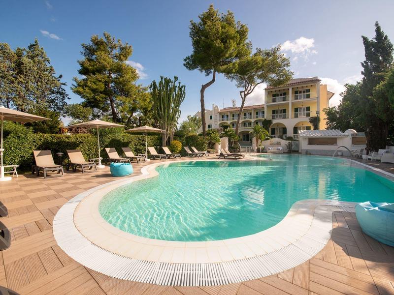 Piscina invitante con lettini e alberi in un giardino dell'hotel al sole.