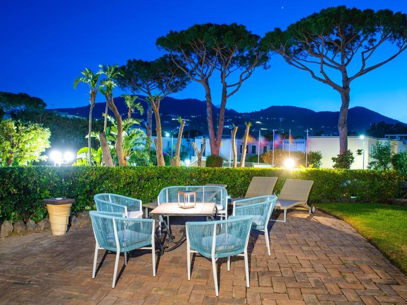 Terrazza serale con zona salotto che si affaccia su giardino illuminato e alberi.