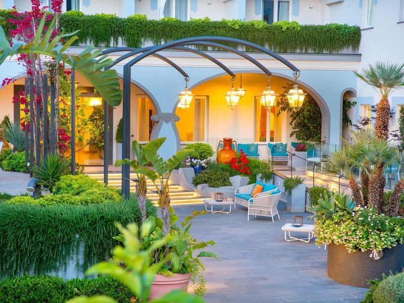 Area salotto illuminata con sedie e piante rigogliose in un cortile d'hotel al crepuscolo