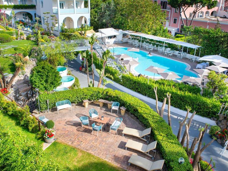 Giardino dell'hotel con aree salotto rotonde e piscina, circondato da palme e verde curato.