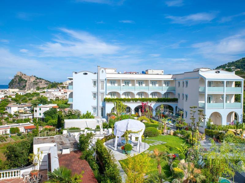 Edificio dell'hotel bianco con camere con balcone e giardino curato con gazebo sotto un cielo limpido.