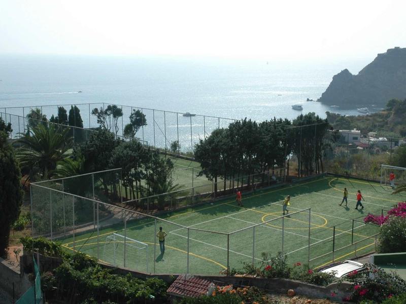 Uitzicht op tennisbaan aan zee met bergen op de achtergrond en spelers op de baan