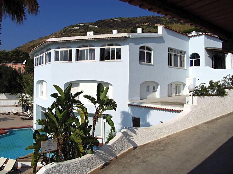 Wit hotelgebouw met bogenramen en een groene buitenzwembad