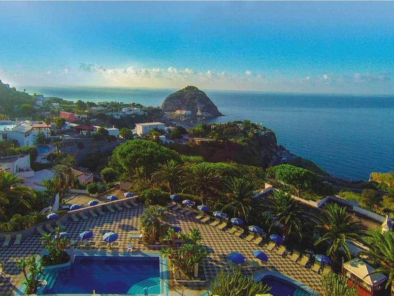 Landschap met hotelcomplex, berg en kust bij zonnige, heldere lucht.