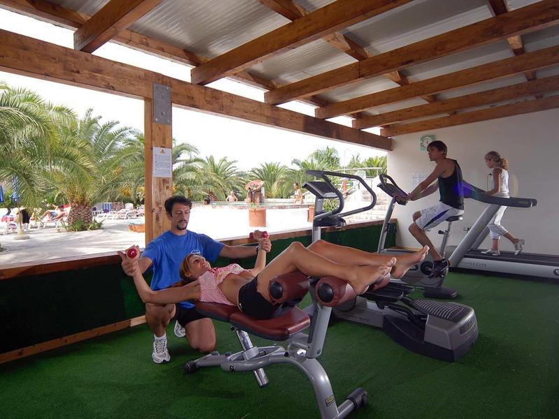 Drie mensen trainen in een overdekte fitnessruimte van een hotel met fitnessapparatuur.