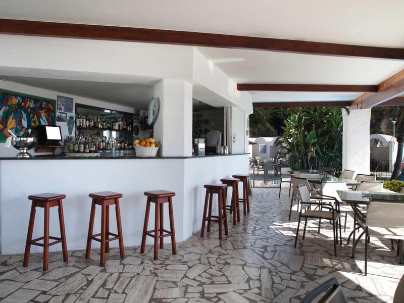 Moderne buitenbar met houten krukken, tafels, lichte tegelvloer en planten.