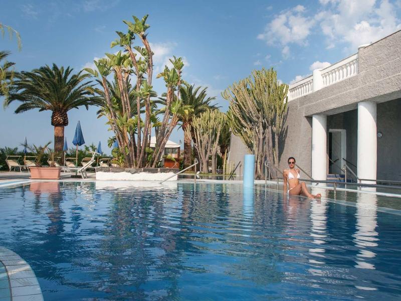 Vrouw ontspant in een hotelzwembad met palmbomen en blauwe lucht.
