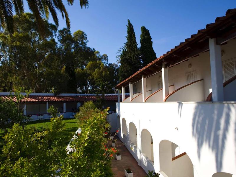 Fasáda budovy s bílými oblouky a palmami na slunné hotelové zahradě.