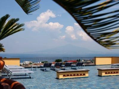 Terrasse mit Sonnenschirmen, Palmen und Blick auf das blaue Meer bei klarem Himmel.