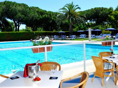 Outdoor-Poolbereich mit Tischen, Stühlen und Sonnenschirmen in einer Hotelanlage.