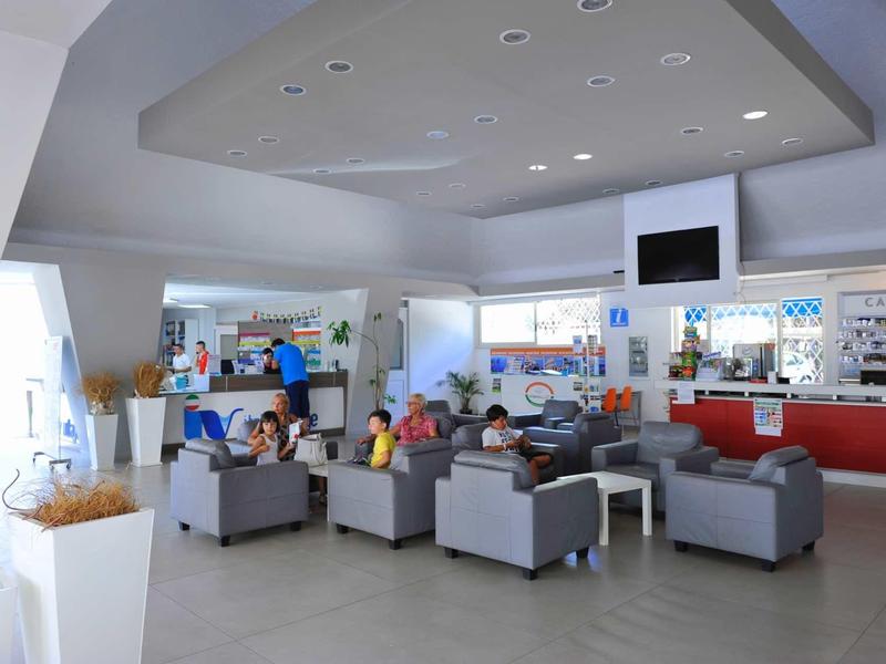 Luminosa lounge dell'hotel con poltrone grigie davanti a una lunga reception e schermo TV