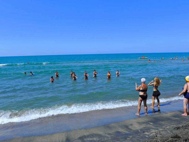 Persone che si divertono a nuotare e giocare in spiaggia con cielo limpido e mare calmo.