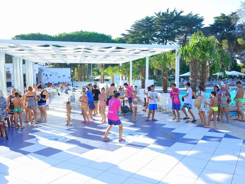 Persone che ballano all'aperto su una terrazza di un hotel soleggiata con palme.