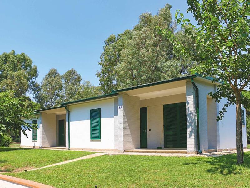 Casa vacanze bianca con porte e persiane verdi in un giardino curato sotto un cielo limpido.