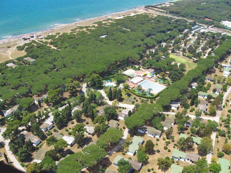 Vista aerea di una località costiera con spiaggia, aree boschive e edifici sparsi.