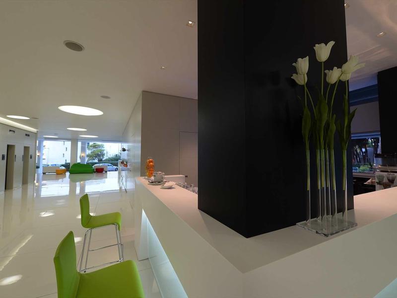 Hall d'hôtel moderne avec comptoir blanc et chaises vertes, fenêtres lumineuses en arrière-plan.