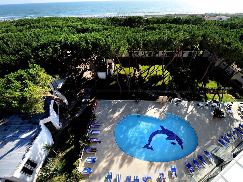 Vue d'une piscine avec mosaïque de dauphins et chaises longues entourée d'arbres près de la mer.