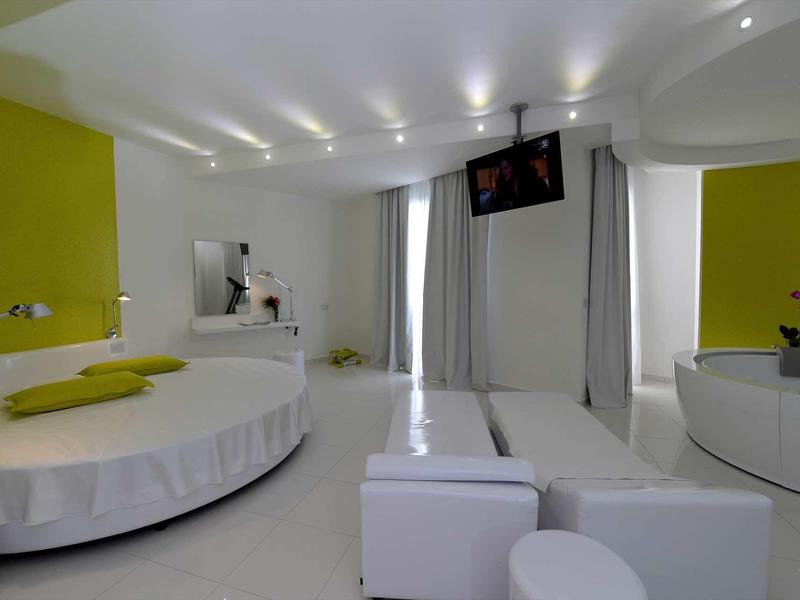 Chambre d'hôtel moderne avec lit rond, intérieur blanc et accents jaunes.