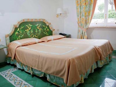 Ložnice s manželskou postelí, zeleným a zlatým čelem a vzorovanou podlahou.