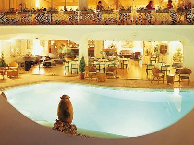 Blick durch eine runde Öffnung auf einen beleuchteten Pool und Sitzbereiche in einem Hotel bei Nacht.