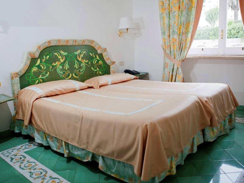 Ložnice s manželskou postelí, zeleným a zlatým čelem a vzorovanou podlahou.