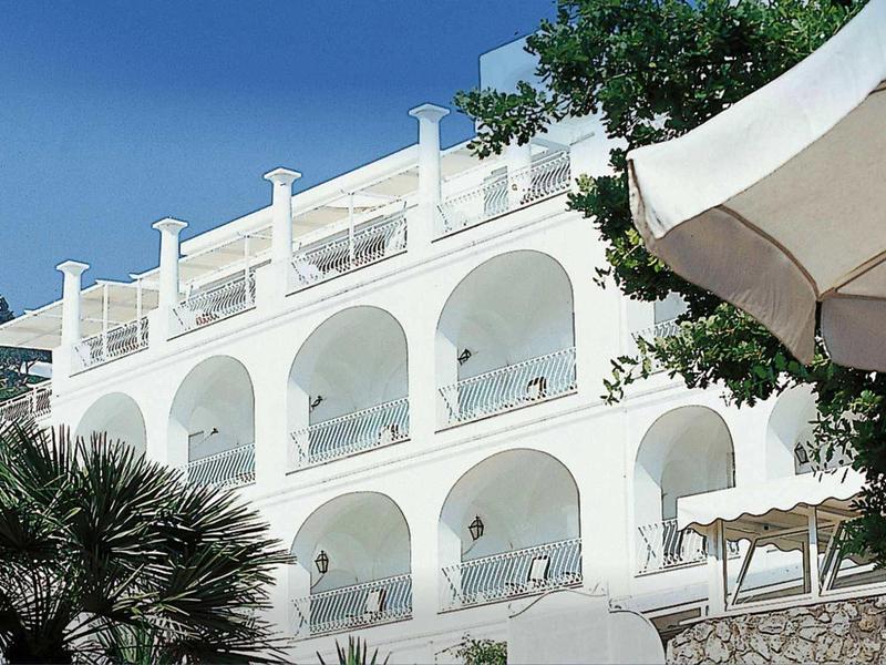 Bílá hotelová budova s obloukovými balkony a venkovním slunečníkem