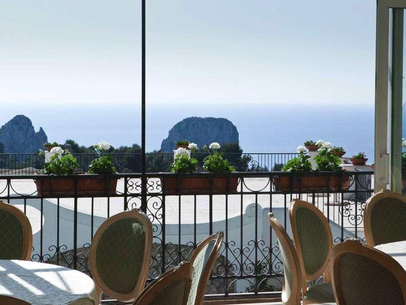 Výhled z restaurace na moře a skály v pozadí za jasné oblohy.