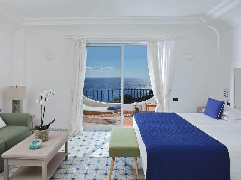 Chambre d'hôtel lumineuse avec lit double, coin salon et vue sur la mer par de grandes fenêtres