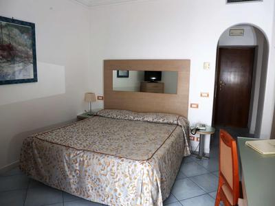 A simply furnished hotel room with a double bed, nightstand, and a desk with a chair.