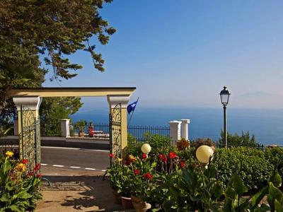 Blick auf das Meer von einem Garten mit Blumen und einem offenen Tor.