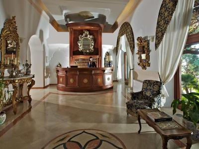 Elegant hotel lobby with antique furniture, high arched ceilings, and large windows overlooking greenery.