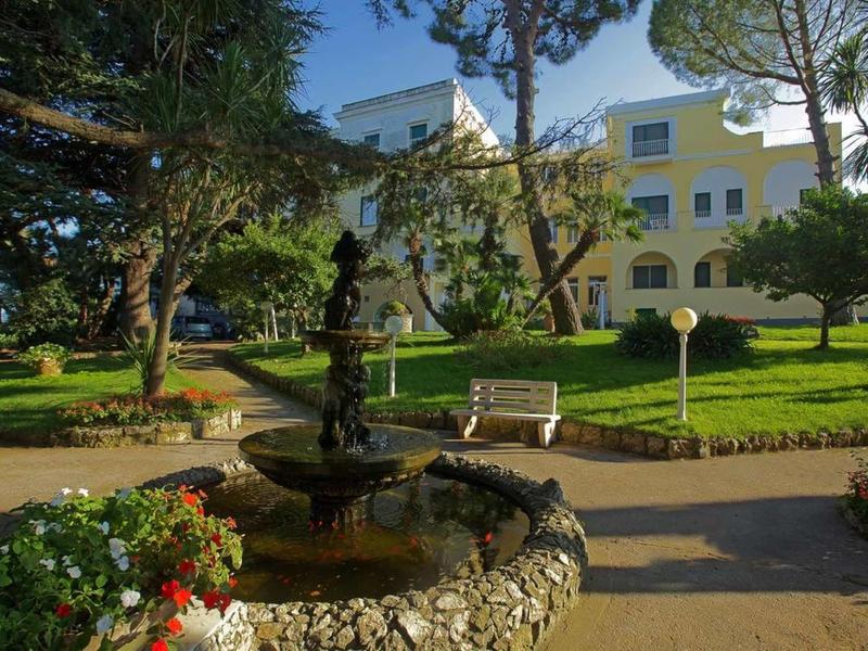 Hotel grounds with fountain, benches, and manicured garden in sunlight