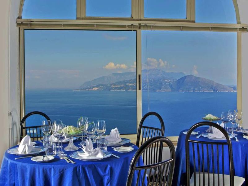 Restaurant with blue tablecloths and view of sea and island under clear sky.