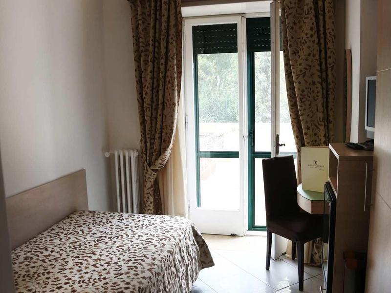 Small bedroom with single bed, desk, and balcony overlooking greenery.