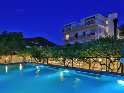 Osvětlený bazén před vícepodlažním domem v noci s horskou krajinou v pozadí.