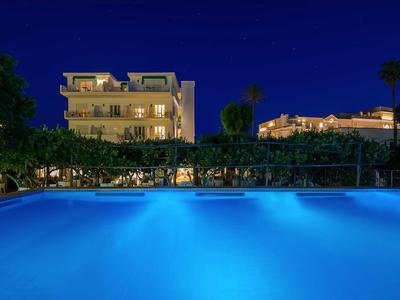 Osvětlený venkovní bazén před hotelovými budovami v noci s jasnou noční oblohou.