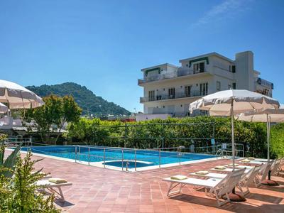 Hotelový bazén s lehátky a slunečníky před budovou pod modrou oblohou.