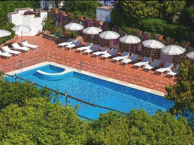 Buitenbad met ligbedden en parasols, omgeven door weelderig groen.