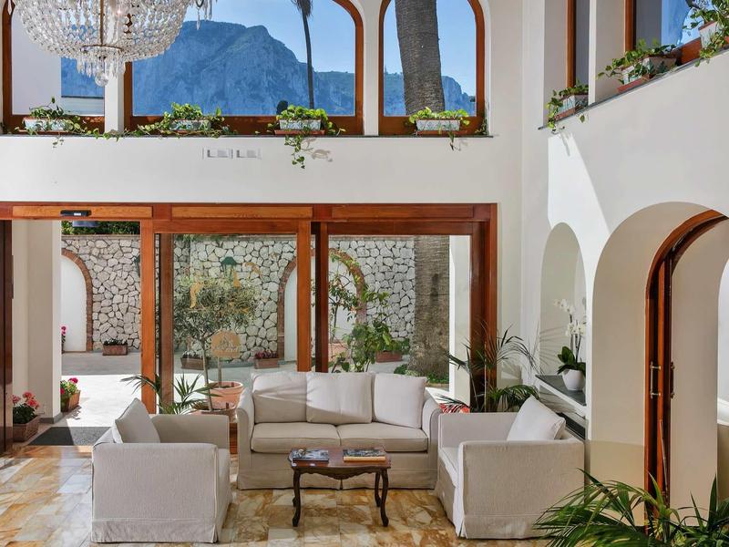 Lichte woonkamer met witte sofa's, planten en grote ramen met uitzicht op de bergen.