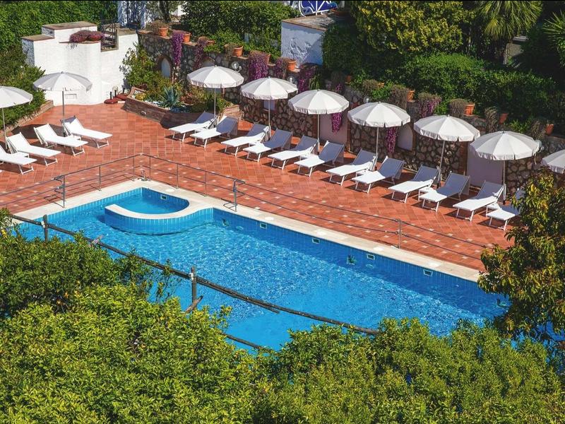 Buitenbad met ligbedden en parasols, omgeven door weelderig groen.