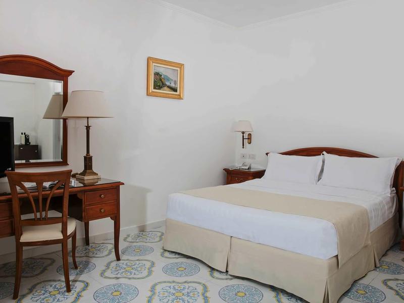 Eenvoudig ingericht hotelkamer met tweepersoonsbed, bureau en stoel.